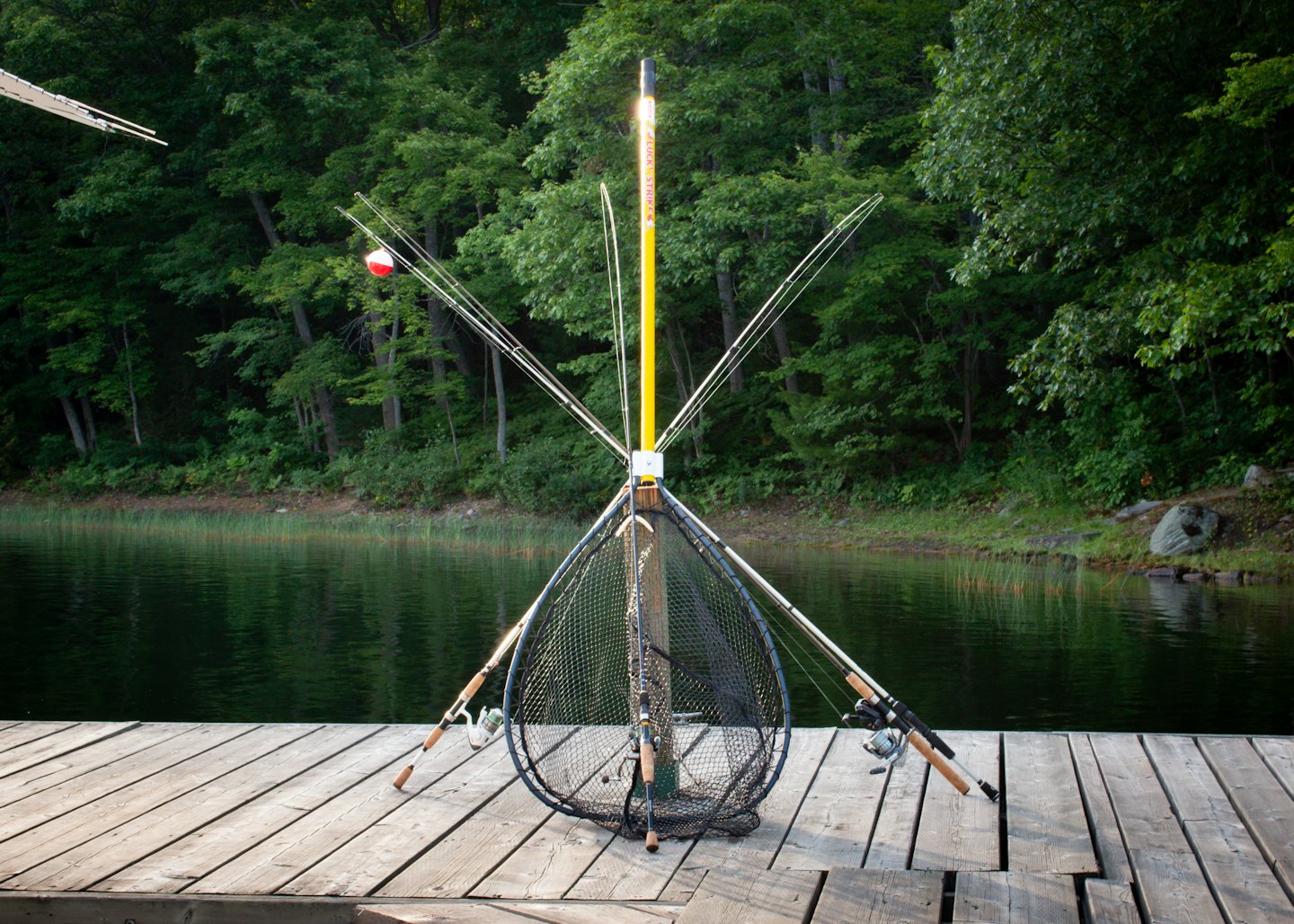 Fishing rods and a net rest against a pole on a wooden dock.
